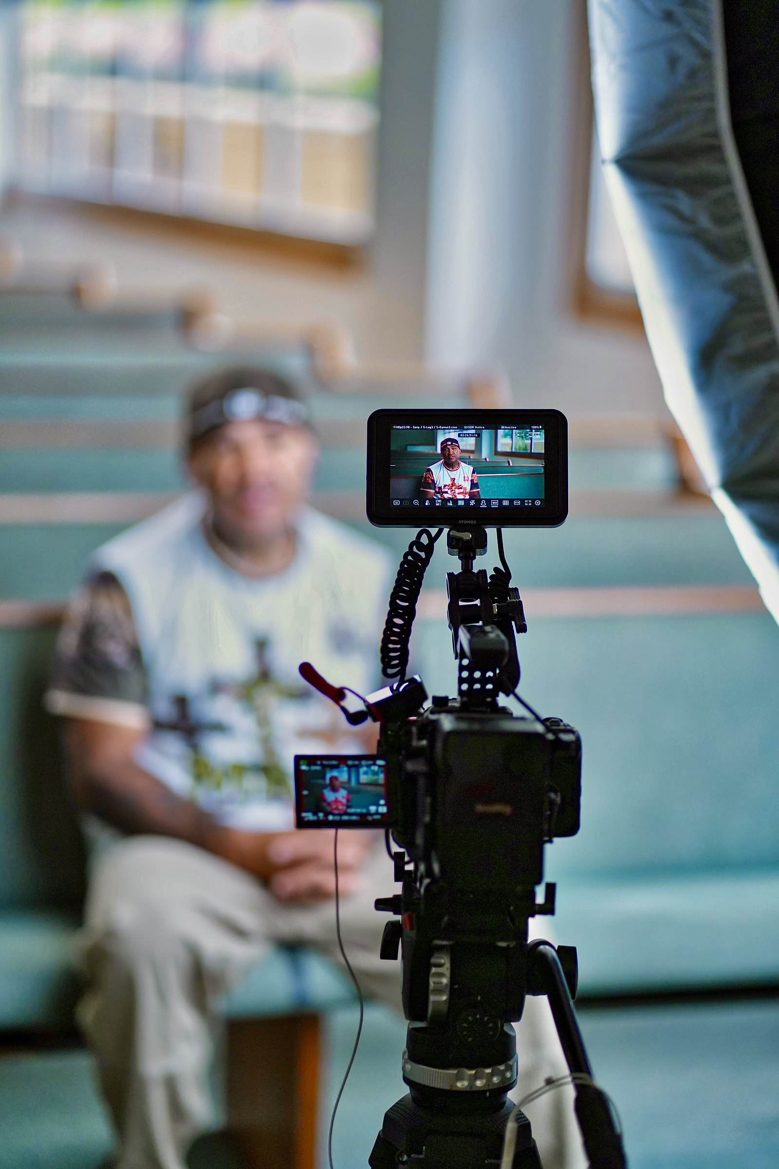 A camera on a tripod, its monitor showing an interview, the subject soft in the background.
