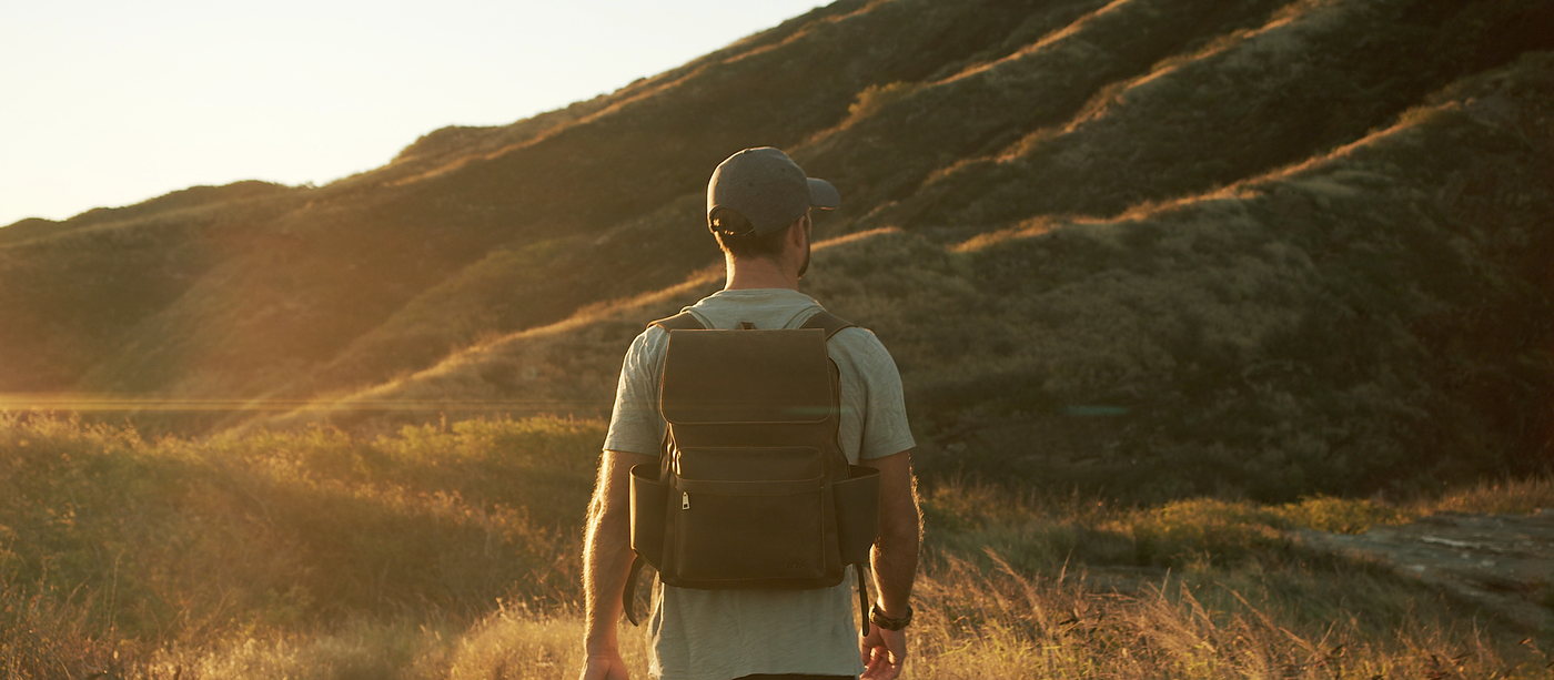 A man with a leather backpack, filmed at golden hour.
