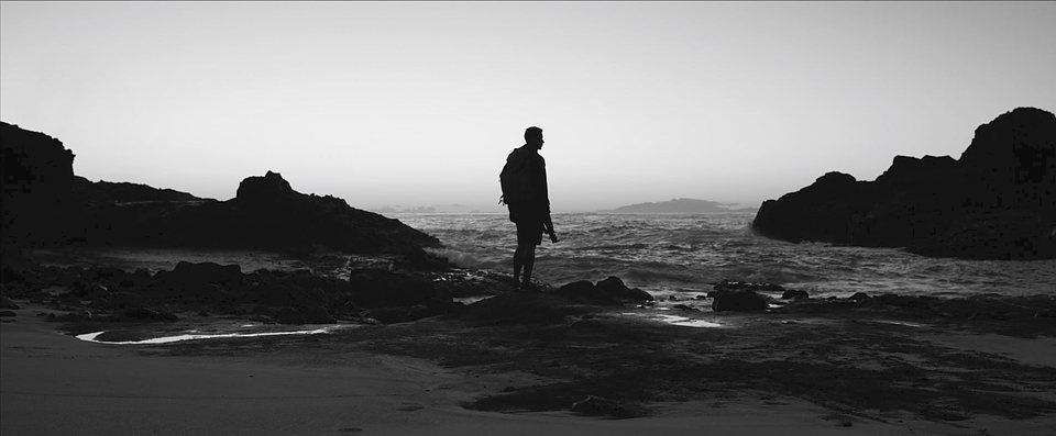A black and white silhouette standing on a beach.